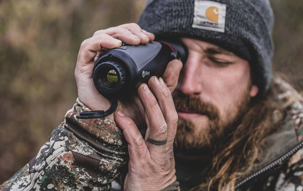 Hunter in a beanie looking through a thermal monocular