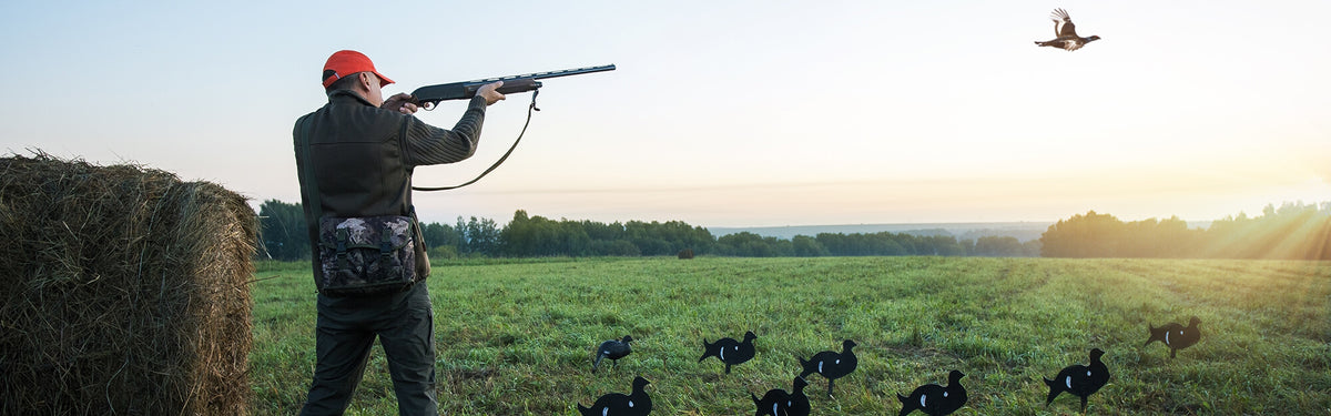 Hunter in a blaze cap firing a shotgun across an open paddock